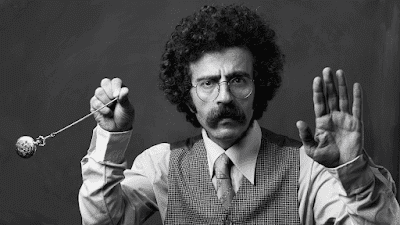 O que é Hipnose: Um homem hipnotizando com um relógio de bolso olhando para camera.